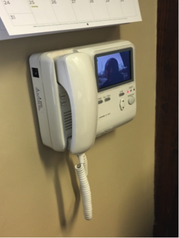 The phone and camera that Ms. Fulcher and Ms. Kretchmar have in their office. This device allows them to see and talk to the person outside, and unlock the door. 