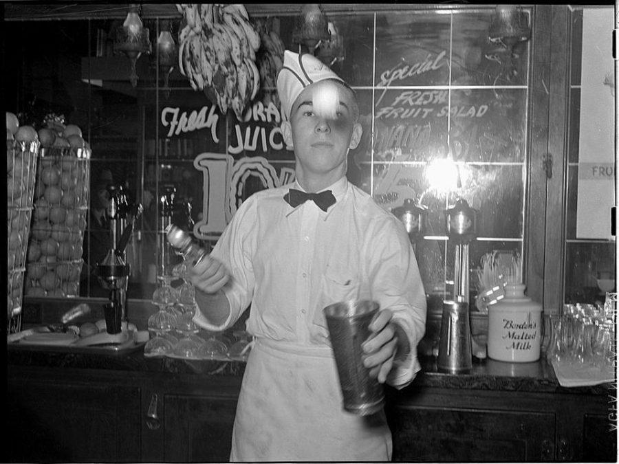 A soda jerk throws a scoop of ice cream into a steel mixing cup while making a milkshake.
Credit: The Library of Congress @ Flickr Commons